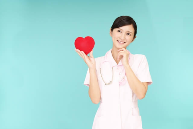 笑顔で赤いハートのイラストを持つ看護師の画像