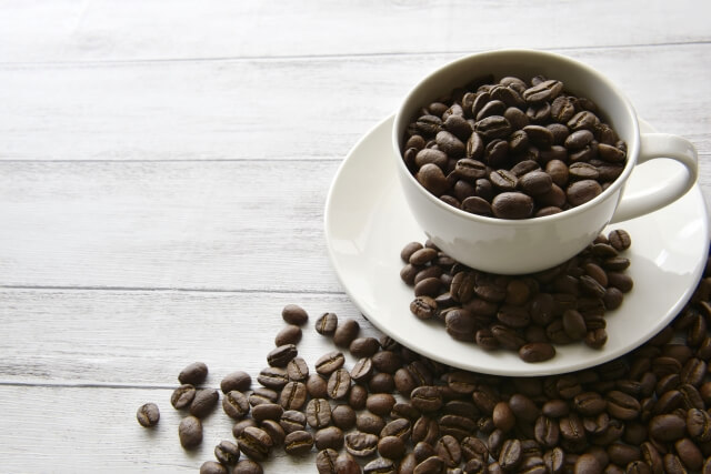 白いコーヒーカップにコーヒー豆があふれている画像