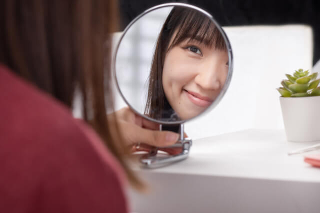 鏡を見て笑顔をつくっている女性の画像