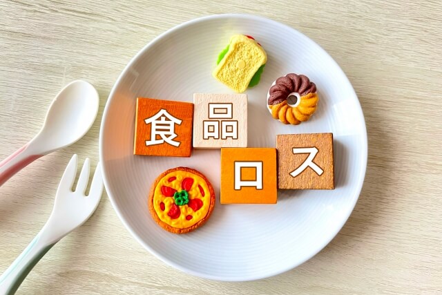 食品ロスのロゴと食べ物のおもちゃが白いお皿の上にのっている画像